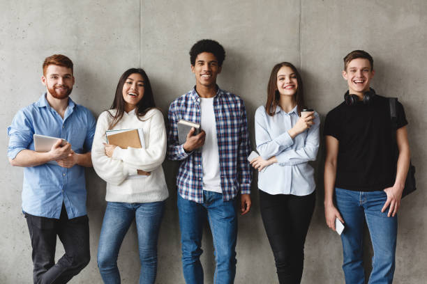 College Students With Books Smiling To Camera Over Grey Wall, Having Break